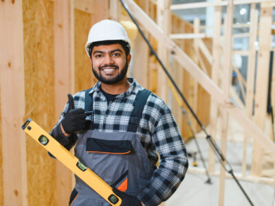 Construction of modular houses. Male Indian construction worker in uniform and hard hat at construction site.
